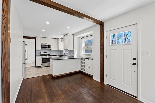 kitchen featuring decorative backsplash, appliances with stainless steel finishes, white cabinetry, a sink, and a peninsula