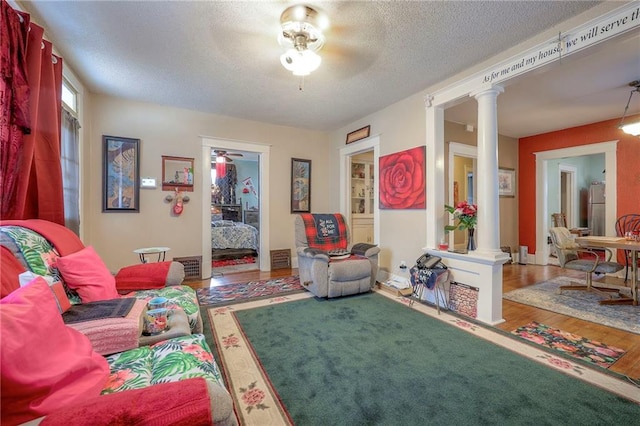 living area featuring ceiling fan, hardwood / wood-style flooring, decorative columns, and a textured ceiling