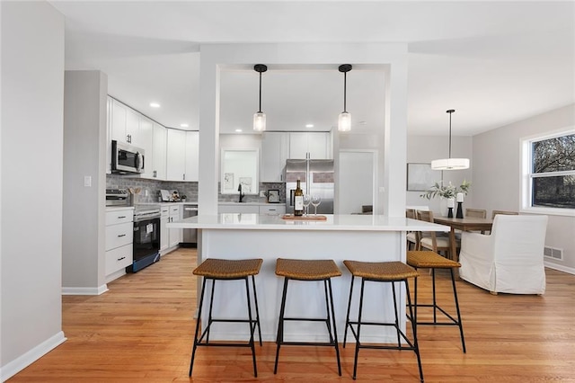 kitchen featuring tasteful backsplash, white cabinets, a breakfast bar area, stainless steel appliances, and light wood-type flooring