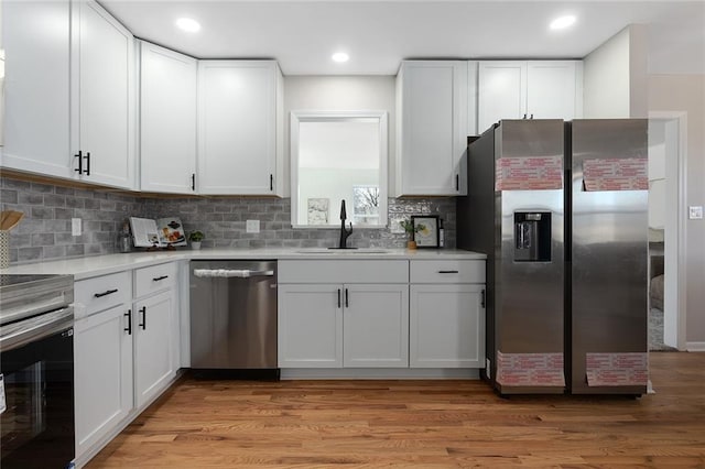 kitchen with stainless steel appliances, light countertops, white cabinetry, a sink, and light wood-type flooring