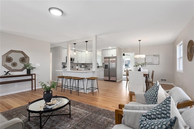 living area with light wood-type flooring, visible vents, and baseboards