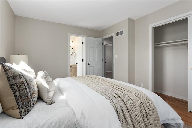 bedroom featuring a closet, visible vents, connected bathroom, wood finished floors, and baseboards