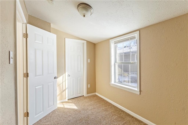 unfurnished bedroom featuring light carpet, lofted ceiling, and a textured ceiling