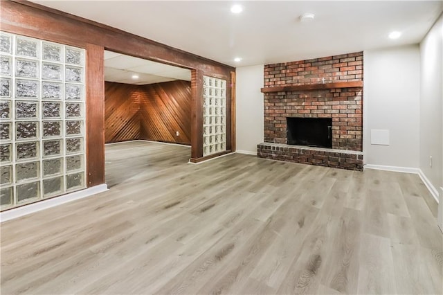 unfurnished living room featuring a brick fireplace, wooden walls, and light hardwood / wood-style floors