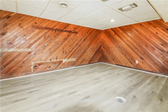 spare room with a paneled ceiling, wooden walls, and hardwood / wood-style floors