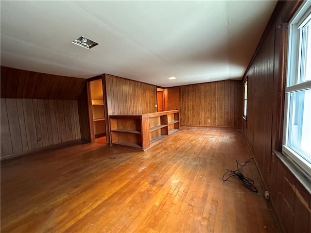 unfurnished living room featuring wood-type flooring, wooden walls, and vaulted ceiling