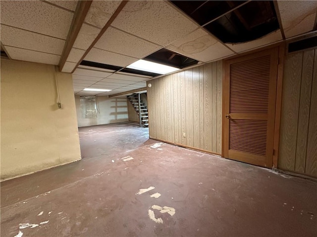 basement featuring a drop ceiling and wooden walls