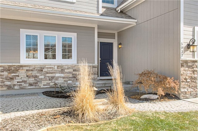 entrance to property with stone siding and a shingled roof