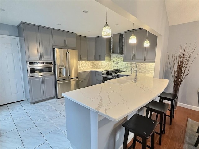 kitchen featuring wall chimney exhaust hood, high quality appliances, gray cabinets, kitchen peninsula, and pendant lighting