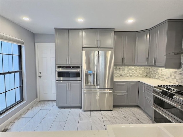 kitchen featuring backsplash, gray cabinets, and appliances with stainless steel finishes