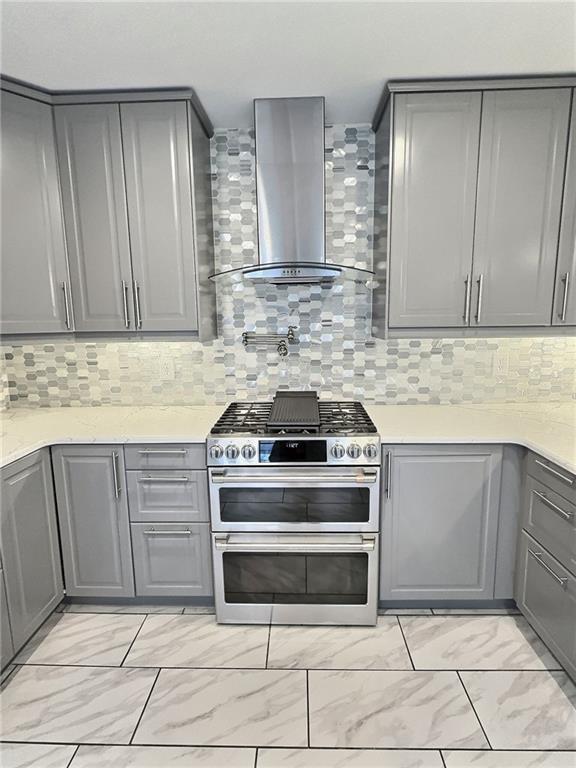 kitchen with gray cabinetry, tasteful backsplash, range with two ovens, and wall chimney range hood