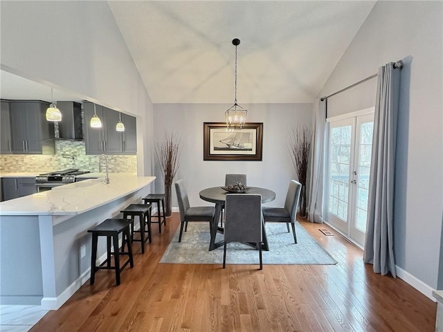 dining space with high vaulted ceiling, sink, hardwood / wood-style flooring, a notable chandelier, and french doors