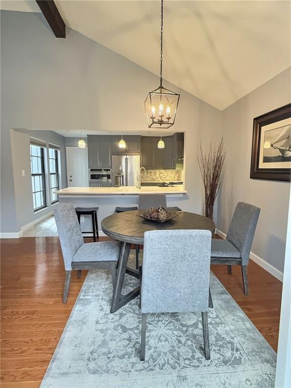 dining area with beamed ceiling, high vaulted ceiling, a chandelier, and light hardwood / wood-style floors