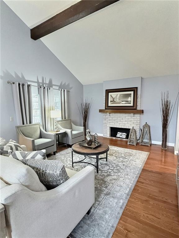 living room featuring wood-type flooring, a brick fireplace, and vaulted ceiling with beams