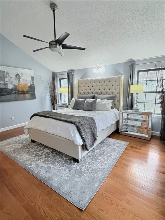 bedroom with hardwood / wood-style floors, vaulted ceiling, a textured ceiling, and ceiling fan