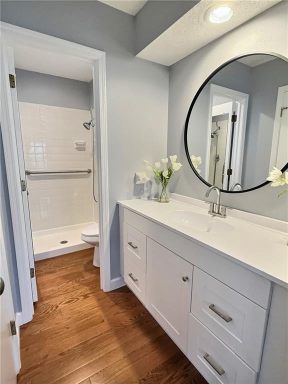 bathroom with tiled shower, vanity, toilet, and hardwood / wood-style floors