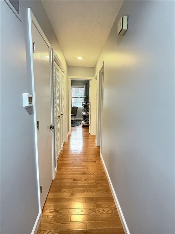 corridor with a textured ceiling and light hardwood / wood-style flooring