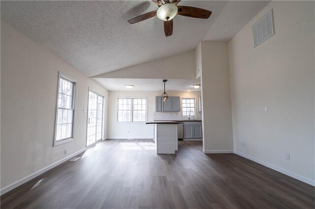 unfurnished living room with ceiling fan, lofted ceiling, dark hardwood / wood-style floors, and a textured ceiling