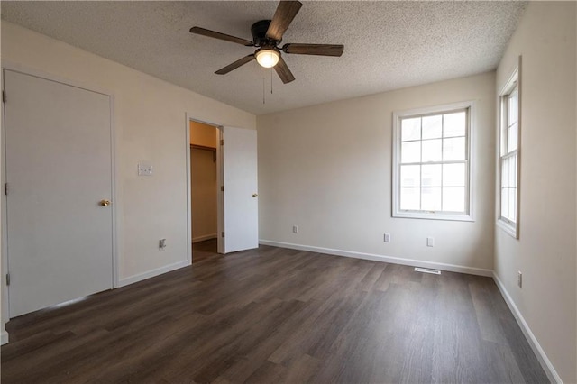 unfurnished bedroom with ceiling fan, dark hardwood / wood-style floors, a textured ceiling, and a spacious closet