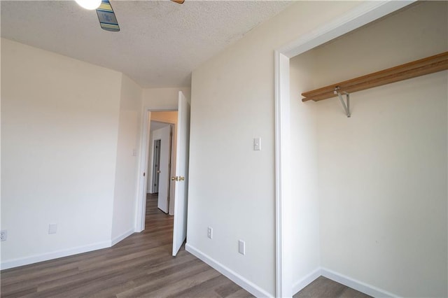 unfurnished bedroom featuring ceiling fan, a closet, dark hardwood / wood-style floors, and a textured ceiling