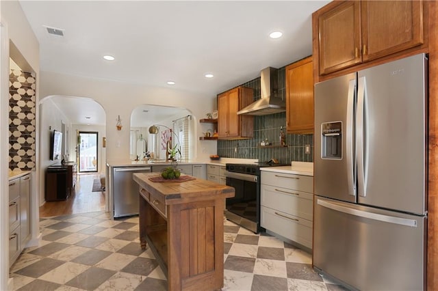 kitchen featuring butcher block countertops, tasteful backsplash, appliances with stainless steel finishes, kitchen peninsula, and wall chimney range hood