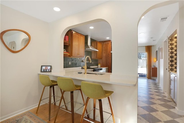 kitchen with sink, backsplash, a kitchen breakfast bar, kitchen peninsula, and wall chimney exhaust hood