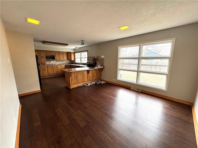 kitchen featuring black fridge, dark wood-type flooring, a textured ceiling, and kitchen peninsula