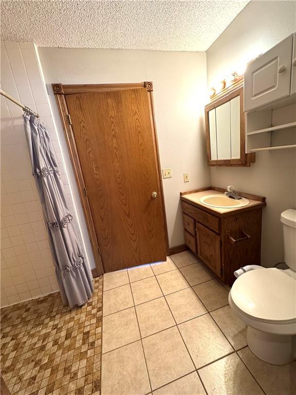 bathroom featuring tile patterned flooring, a shower with shower curtain, vanity, a textured ceiling, and toilet