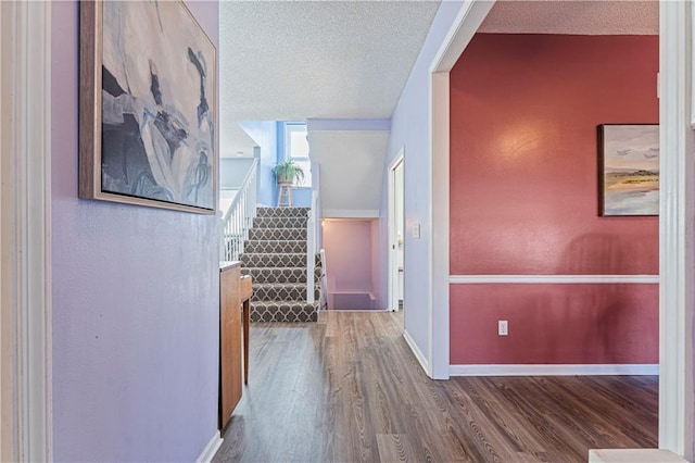 corridor featuring baseboards, a textured ceiling, wood finished floors, and stairs