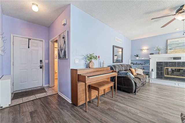 entryway featuring visible vents, dark wood-type flooring, a tiled fireplace, a textured ceiling, and ceiling fan