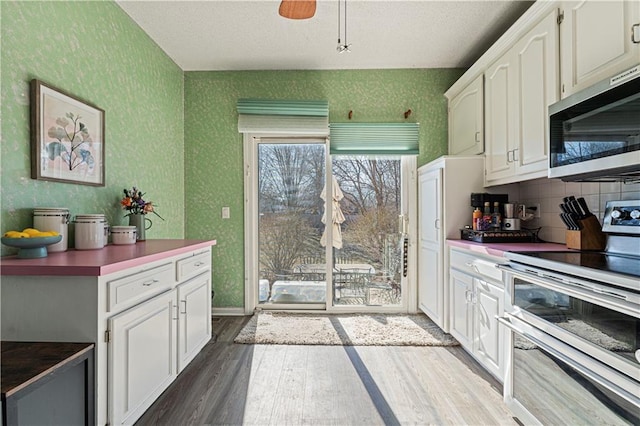 kitchen with wallpapered walls, white cabinets, dark wood finished floors, and stainless steel appliances