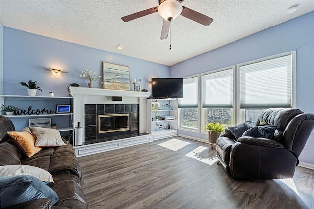 living area featuring a textured ceiling, wood finished floors, a ceiling fan, and a tiled fireplace