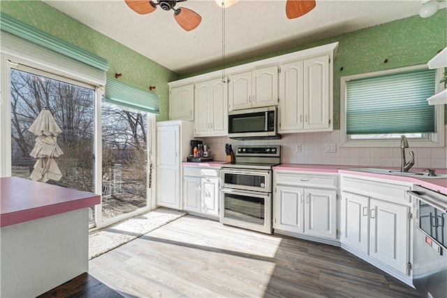 kitchen with a sink, stainless steel appliances, a ceiling fan, and wallpapered walls