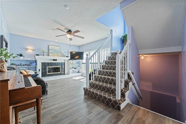 staircase with a tiled fireplace, a textured ceiling, a ceiling fan, and wood finished floors