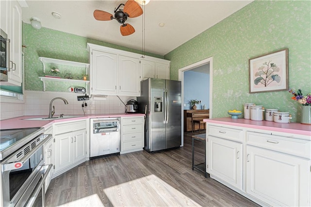 kitchen with a sink, wood finished floors, white cabinetry, appliances with stainless steel finishes, and wallpapered walls