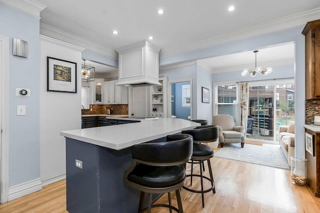 kitchen featuring white cabinetry, a kitchen breakfast bar, ornamental molding, decorative light fixtures, and a chandelier