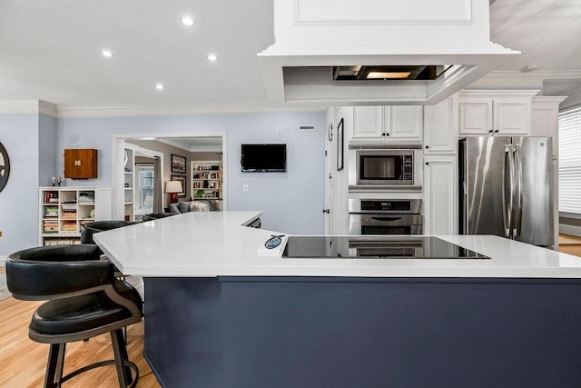 kitchen with appliances with stainless steel finishes, a breakfast bar, white cabinets, crown molding, and light wood-type flooring