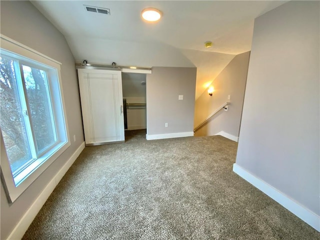 carpeted empty room with a barn door and vaulted ceiling