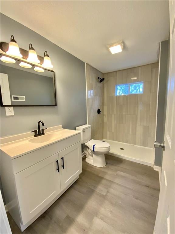 bathroom featuring vanity, toilet, hardwood / wood-style floors, and a tile shower