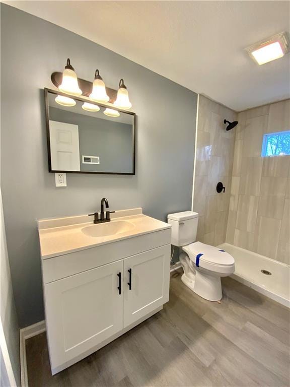 bathroom featuring hardwood / wood-style flooring, vanity, a tile shower, and toilet