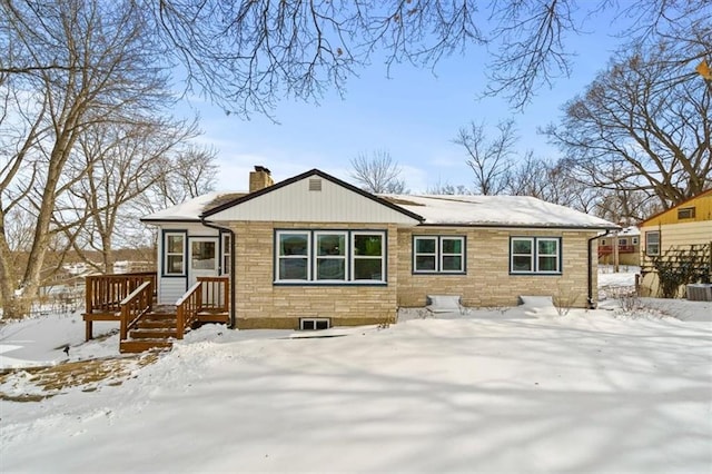 snow covered house with stone siding, a chimney, and a deck