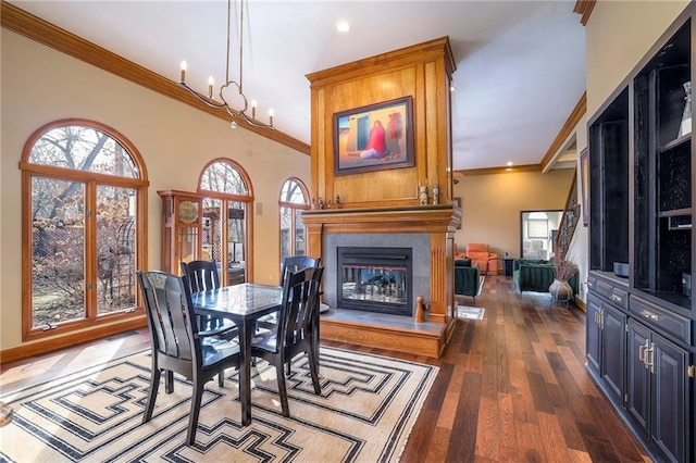 dining area featuring a large fireplace, crown molding, an inviting chandelier, and wood finished floors