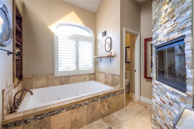 bathroom with visible vents, toilet, a whirlpool tub, tile patterned flooring, and a stone fireplace