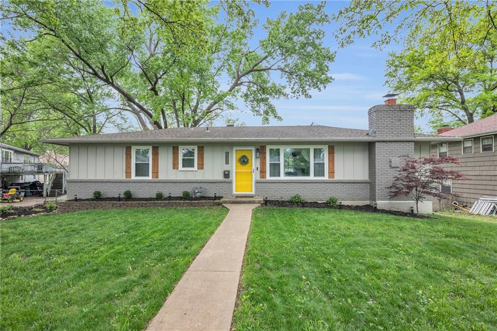 ranch-style home featuring board and batten siding, a chimney, a front lawn, and brick siding