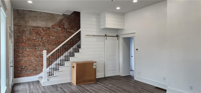 stairs featuring wood finished floors, baseboards, brick wall, recessed lighting, and a barn door