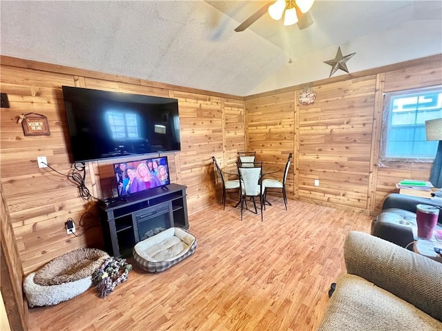 living room featuring ceiling fan, wood-type flooring, wooden walls, and vaulted ceiling