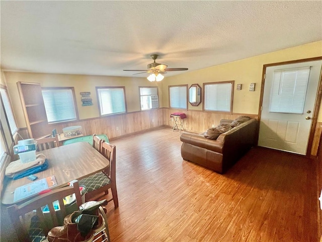 living room with ceiling fan, light hardwood / wood-style flooring, a textured ceiling, and wood walls