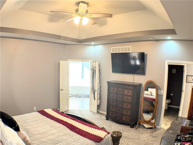 carpeted bedroom featuring a raised ceiling, ceiling fan, and ensuite bath