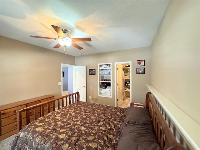 carpeted bedroom with a textured ceiling, a walk in closet, and ceiling fan