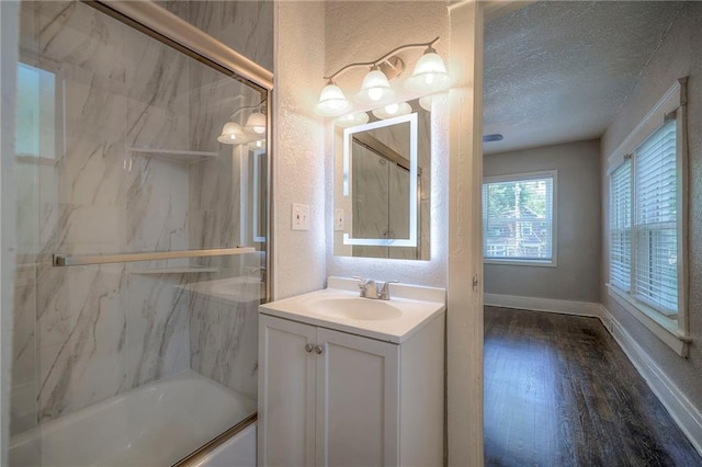 bathroom with wood-type flooring, combined bath / shower with glass door, vanity, and a textured ceiling